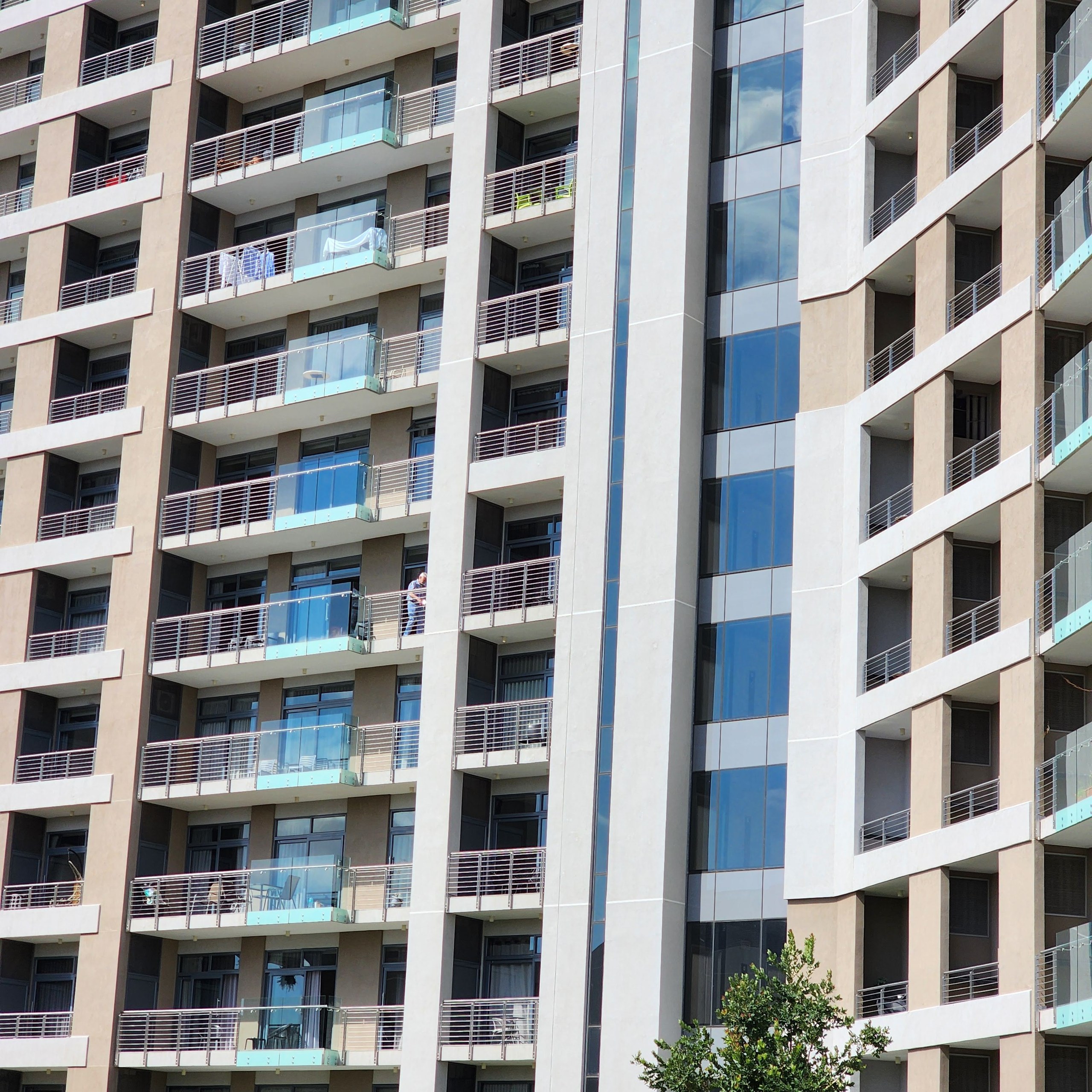 Occupied apartment tower shot tight: rows of recessed balconies with wire balustrades and glass screens, with the pale render coating carried across every soffit, balcony wall and horizontal band.