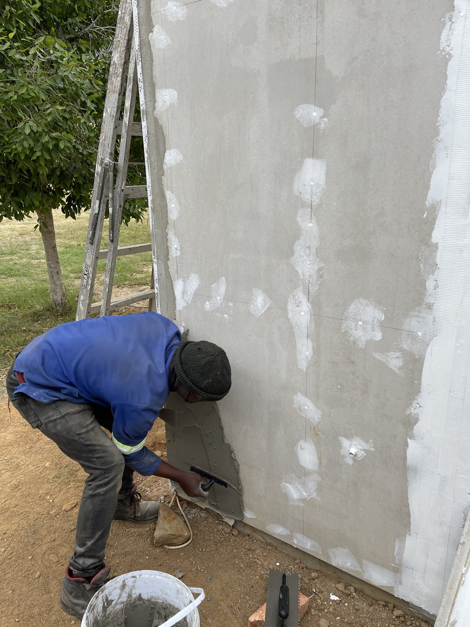 Trowelling basecoat onto an EPS board wall section, mesh and disc fixings visible at the edges