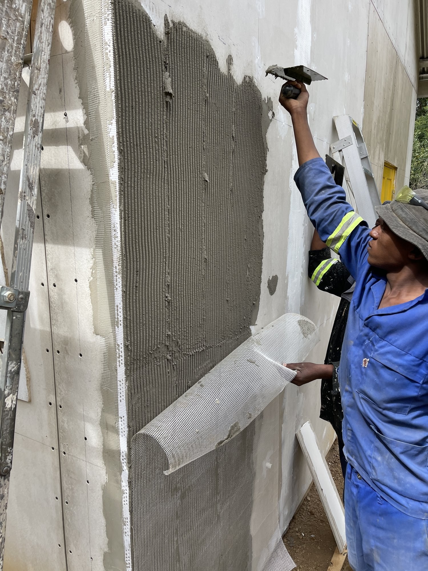 Worker embedding fibreglass mesh into wet basecoat at an external wall corner