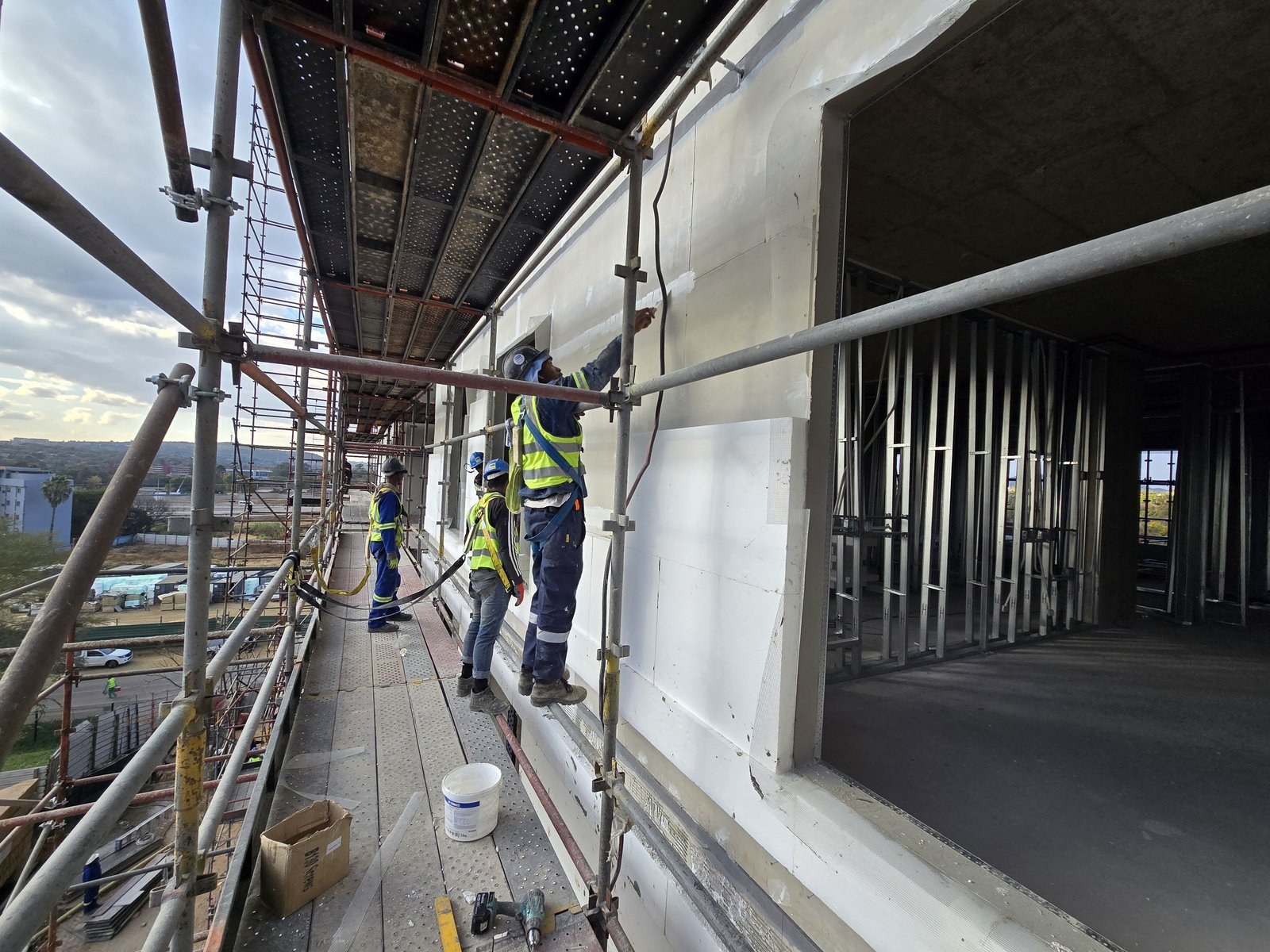 Workers applying basecoat to EPS boards from a scaffold platform on a high-rise facade