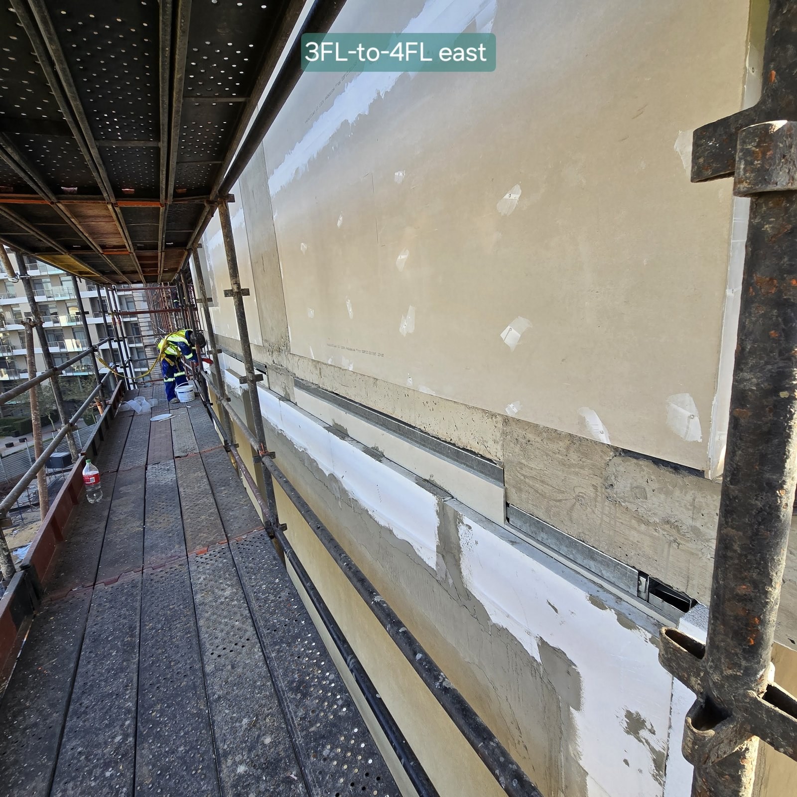 Worker finishing render between the 3rd and 4th floor on a scaffold walkway