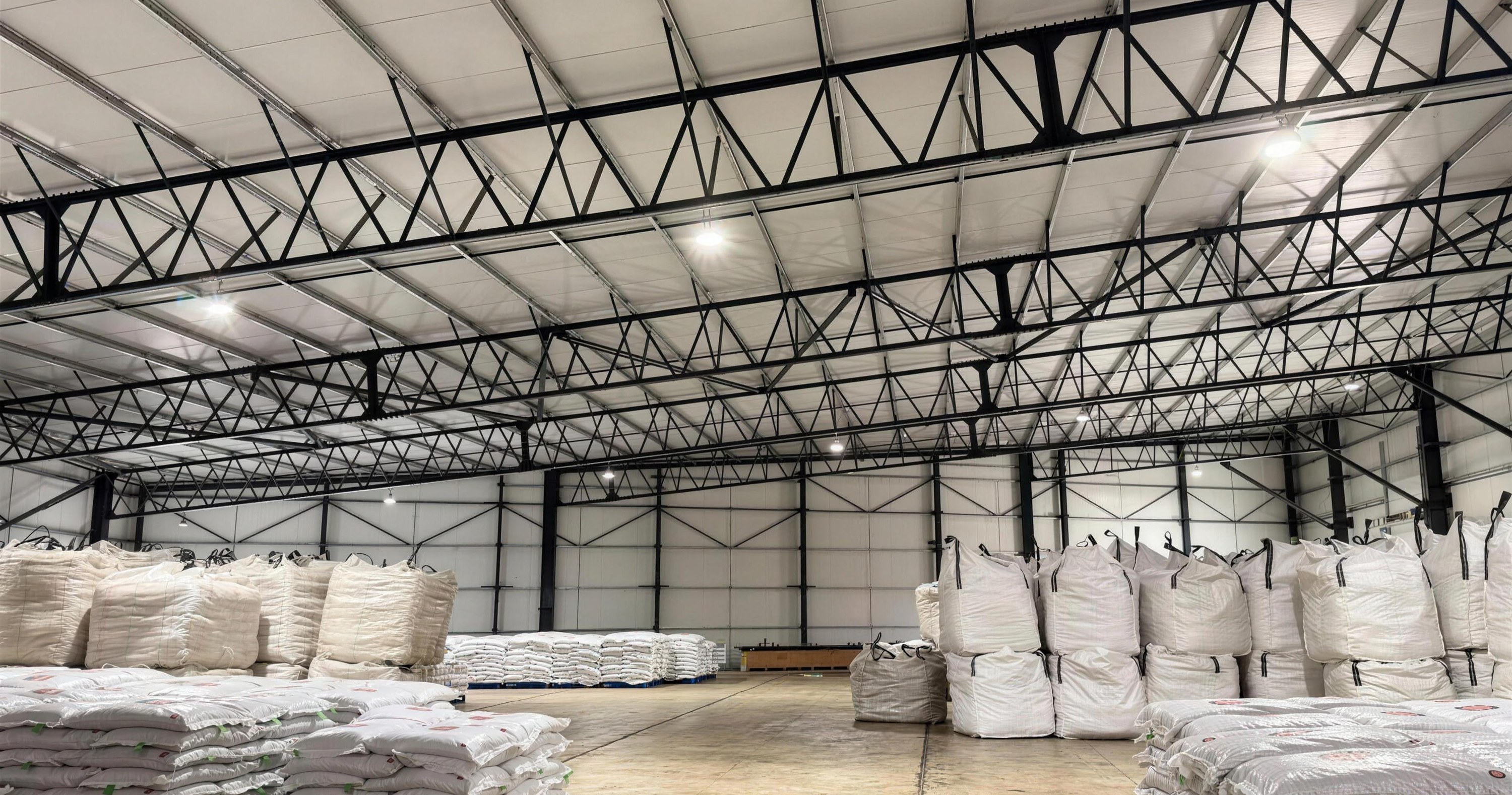 Inside a completed Technopol insulated building on the Swiss greenhouse project: a clear-span steel truss roof lined with steel-faced insulated panels, stacked product on the floor below
